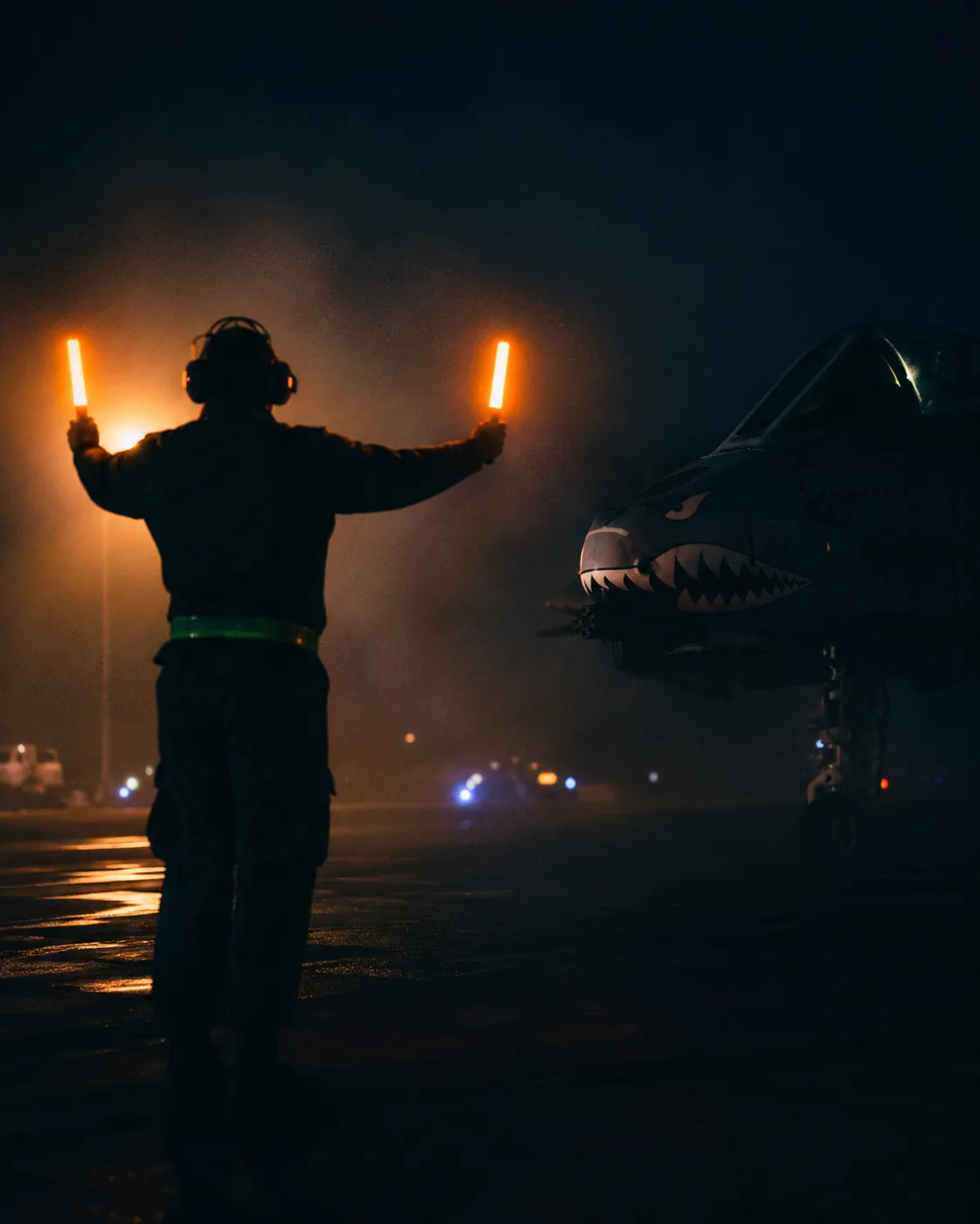 Marshaller guiding an A-10 with lit wands at night